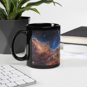 Puede incluir: Taza de cerámica negra con una imagen colorida de una nebulosa, una nube de gas y polvo en el espacio, impresa en la parte delantera.