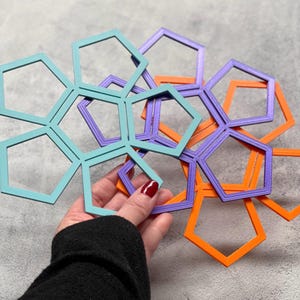 May include: A collection of colorful geometric shapes in teal, purple, and orange. The shapes are pentagons connected to each other, creating a complex, layered design. The image is taken from a close-up perspective, highlighting the vibrant colors and intricate details.