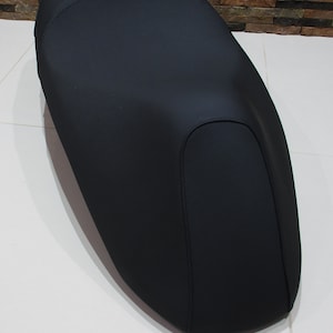 May include: Black motorcycle seat with a single, deep, rounded indentation. The seat is made of a smooth, textured material.
