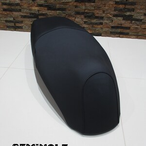 May include: Black motorcycle seat with a smooth, slightly curved surface. The seat is made of a durable material and has a simple, classic design.