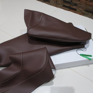 May include: Three brown leather car seat covers with white stitching. The covers are folded and placed on a white box with a green tag that says "Remarkable".