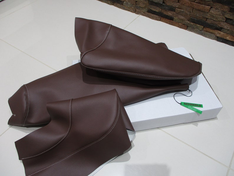 May include: Three brown leather car seat covers with white stitching. The covers are folded and placed on a white box with a green tag that says "Remarkable".