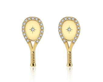 May include: A pair of gold tennis racket earrings with a single diamond in the center of each racket. The rackets are surrounded by a circle of smaller diamonds.
