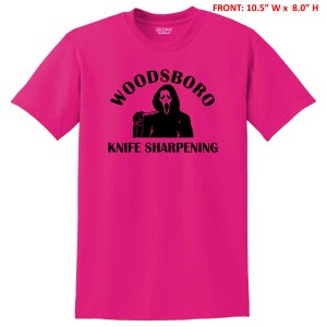 May include: Pink t-shirt with a black graphic of a ghost holding a knife and the text "Woodsboro Knife Sharpening".
