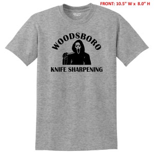 May include: A gray t-shirt with a black graphic of a ghost holding a knife and the text "Woodsboro Knife Sharpening".