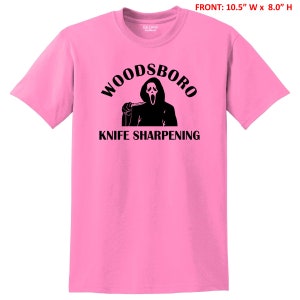 May include: Pink t-shirt with a black graphic of a ghost holding a knife and the text "Woodsboro Knife Sharpening".