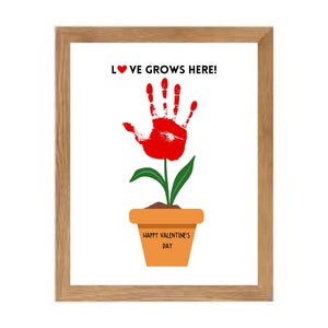 May include: A framed print with a red handprint shaped like a flower in a pot. The text "LOVE GROWS HERE!" is above the flower and "HAPPY VALENTINE'S DAY" is on the pot.