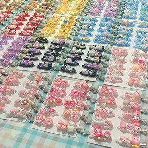 May include: A collection of colorful hair clips featuring various cartoon characters and designs. The clips are arranged in rows on a white and blue checkered surface.