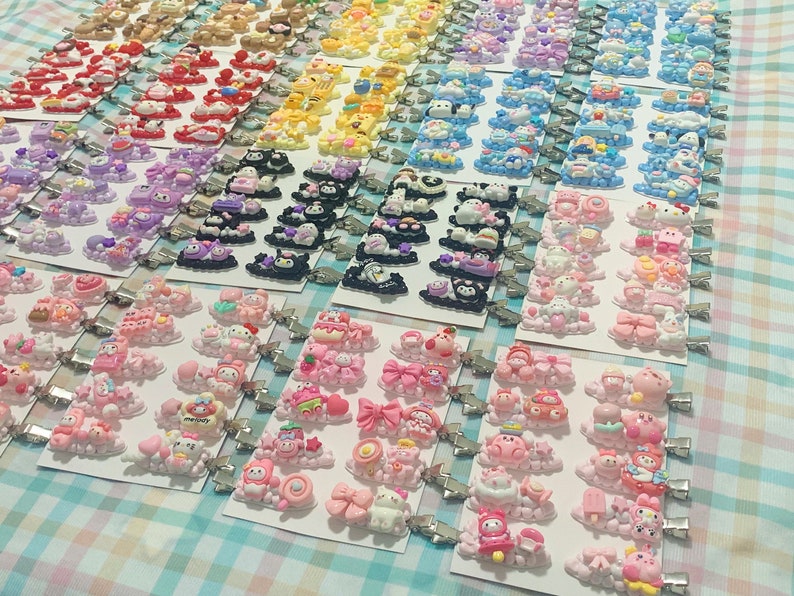 May include: A collection of colorful hair clips featuring various cartoon characters and designs. The clips are arranged in rows on a white and blue checkered surface.
