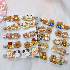 May include: A set of 20 colorful hair clips featuring various cartoon animal designs, including bears, dogs, and a cow. The clips are decorated with different food and drink items, such as chocolate, strawberries, and milk bottles. The clips are arranged on a white background with the text "Happy Farm" on one of the clips.