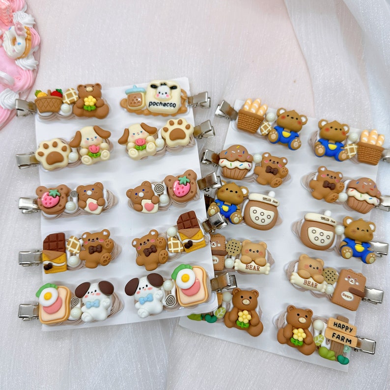 May include: A set of 20 colorful hair clips featuring various cartoon animal designs, including bears, dogs, and a cow. The clips are decorated with different food and drink items, such as chocolate, strawberries, and milk bottles. The clips are arranged on a white background with the text "Happy Farm" on one of the clips.