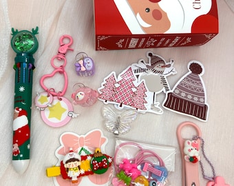 May include: A Christmas-themed gift set including a multi-color pen with a green topper, a pink heart keychain, small hair clips, stickers of a snowman and trees, a butterfly charm, hair ties, and pink nail clippers with a rabbit charm.