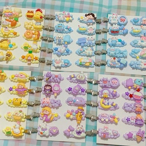 May include: A collection of colorful hair clips with various cartoon characters and designs. The clips are attached to silver metal clips and feature a variety of themes, including animals, food, and flowers.