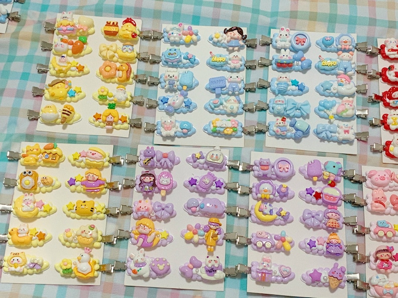 May include: A collection of colorful hair clips with various cartoon characters and designs. The clips are attached to silver metal clips and feature a variety of themes, including animals, food, and flowers.
