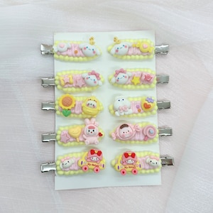 May include: A set of 12 colorful hair clips featuring various cartoon characters. The clips are made of plastic and have a metal clip on the back. The characters include a bunny, a bear, a sunflower, and a car.