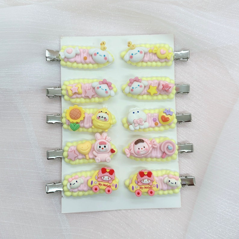 May include: A set of 12 colorful hair clips featuring various cartoon characters. The clips are made of plastic and have a metal clip on the back. The characters include a bunny, a bear, a sunflower, and a car.