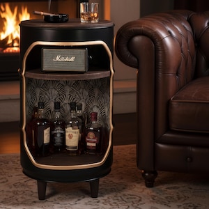 May include: A black barrel-shaped side table with a wooden top, featuring a built-in shelf with liquor bottles and a Marshall speaker. The table has a gold trim and sits on dark wooden legs. A glass of whiskey and an ashtray with a cigar are on top.