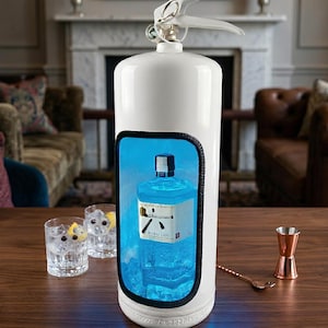 Può includere: Un estintore bianco riadattato a mobile bar con un'apertura rettangolare che mostra una bottiglia di Roku Gin illuminata da una luce blu. Due bicchieri trasparenti con ghiaccio e fette di limone e un misurino in rame sono posati sul tavolo.
