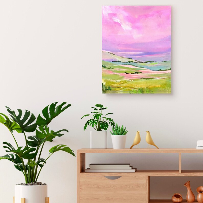 Puede incluir: Una pintura de un paisaje con colinas onduladas y un cielo rosa. Las colinas est&aacute;n pintadas en tonos de verde, rosa y amarillo. El cielo es de un rosa vibrante con nubes blancas.