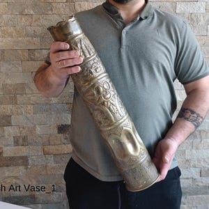 Op de afbeelding: Een messing vaas met ingewikkelde houtsnijwerk, waarschijnlijk gemaakt van een hergebruikte artilleriegranaat. De vaas is versierd met bloem- en geometrische patronen.  Trench Art Vase_1