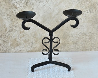 May include: Black metal candle holder with two arms and a decorative base. The holder has a scrolled design and is perfect for displaying candles.