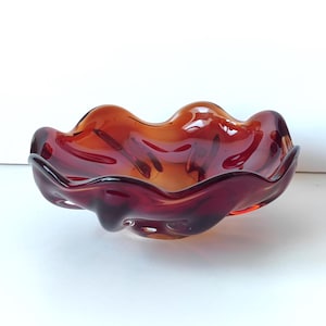 May include: A red and amber glass bowl with a wavy, organic shape. The bowl is made of thick glass and has a glossy finish.
