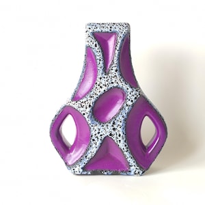 Puede incluir: Un jarrón decorativo de cerámica con un diseño único. El jarrón presenta un color púrpura vibrante con un patrón texturizado, moteado blanco y negro. El jarrón tiene una forma abierta y geométrica con recortes redondeados.