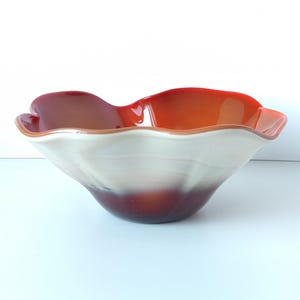 Puede incluir: Un cuenco de vidrio con bordes ondulados, interior blanco y exterior rojo y naranja.