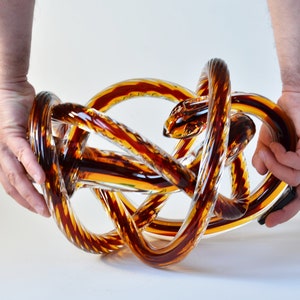 Peut inclure: Une sculpture en verre en forme de nœud, avec un schéma de couleurs brun et clair.