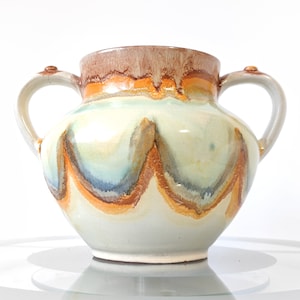May include: A white ceramic vase with two handles. The vase has a brown, orange, and blue glaze with a wavy pattern.