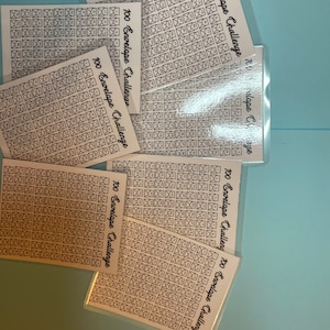 Może przedstawiać: Zestaw ośmiu białych kart z czarnymi zarysami kopert. Na każdej karcie znajduje się napis "100 Envelope Challenge".