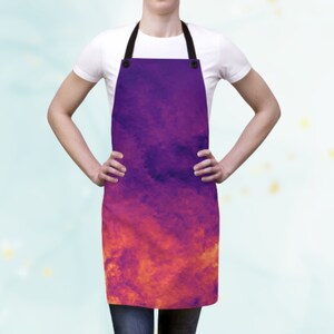 Könnte beinhalten: Eine Schürze mit einem lebendigen, abstrakten Design. Die Schürze zeigt einen Farbverlauf, der von tiefem Lila oben nach feurigem Orange unten übergeht. Sie hat einen schwarzen Nackenriemen und wird von einer Person getragen.
