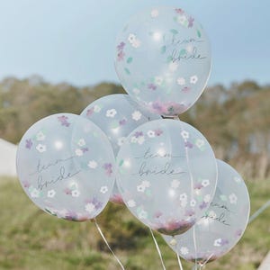 Könnte beinhalten: Eine Gruppe klarer Ballons mit floralem Konfetti und dem Schriftzug "team bride". Die Ballons sind mit kleinen Blumen in Lila, Rosa und Grün verziert, ideal für eine Brautparty oder Hochzeitsfeier.
