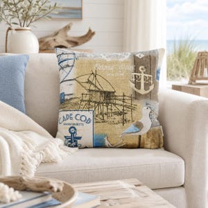 Könnte beinhalten: Ein quadratisches Dekokissen mit nautischem Motiv auf beigem Hintergrund. Das Design zeigt eine schwarze Strichzeichnung einer Fischereianlage, eine weiße Möwe, einen blauen Anker sowie den Text Cape Cod Massachusetts und Original Spirit.