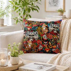 May include: A decorative square cushion with a tattoo-style design. The cushion showcases skulls, tigers, roses, and hearts in a colourful collage. The design incorporates text elements and is set against a black backdrop.
