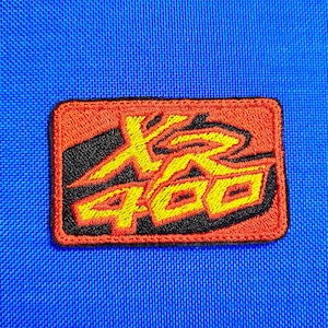 May include: A rectangular patch with an orange border and a black background. The patch features yellow text that reads "400" and a stylized design. The patch is set against a blue fabric background.