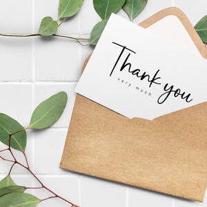 May include: A white card with the text "Thank you very much" in black calligraphy, inside a brown paper envelope. The card and envelope are on a white tiled surface with green leaves.