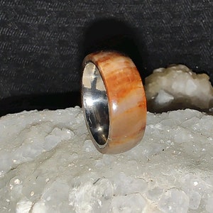 May include: A ring with a brown and white wood inlay and a silver band.