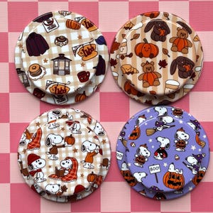 May include: Four circular phone grips featuring various patterns. The top left has a tan gingham print with coffee shop icons. The top right has a tan gingham print with bears and pumpkins. The bottom left has a tan gingham print with cartoon dogs. The bottom right has a purple background with cartoon dogs and pumpkins.