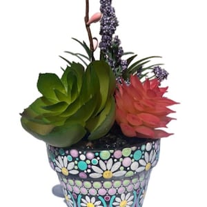 Op de afbeelding: Een kleine, zwarte terracotta pot beschilderd met witte madeliefjes en kleurrijke stippen. De pot is gevuld met kunstmatige vetplanten en lavendel.