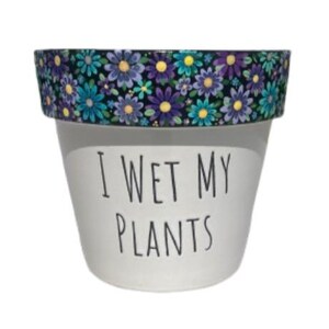 May include: White ceramic plant pot with the text "I WET MY PLANTS" in black. The rim of the pot is decorated with a floral pattern featuring blue, purple, and yellow flowers on a black background. A decorative item for plant lovers.