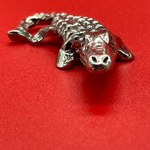 May include: A silver alligator figurine with a detailed textured surface. The alligator is posed with its head raised and mouth closed.