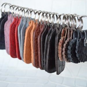 May include: A collection of leather keychains in various colors and textures, including brown, black, red, and gray. The keychains are hanging on metal rings.
