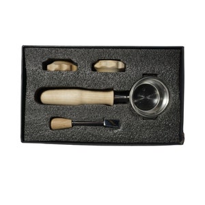 May include: A black box with a foam interior containing a coffee tamper, a tamper tool, and two wooden tamper bases.