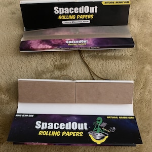 Puede incluir: Un paquete de papeles de liar SpacedOut King Slim Size con un extraterrestre verde y un gráfico de OVNI. Los papeles son sin blanquear y hechos con goma arábiga natural.