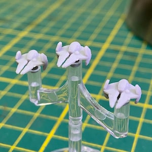 Puede incluir: Tres naves espaciales en miniatura de color púrpura se muestran en un soporte de plástico transparente. El soporte tiene tres brazos que se extienden desde una base central.