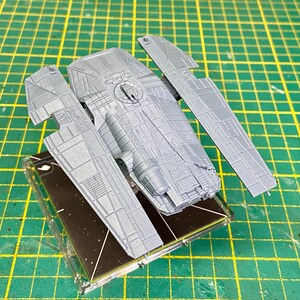 May include: A grey plastic model of a spaceship with two wings. The spaceship is sitting on a black base with a star pattern.