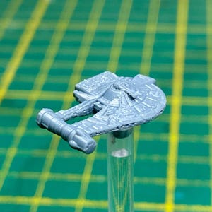 May include: A grey plastic model of a spaceship with a rounded cockpit and two wings. The model is on a clear plastic rod.