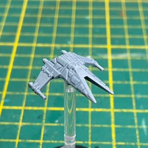 May include: A gray plastic model of a starfighter spaceship with a pointed nose and two wings. The model is mounted on a clear plastic stand.