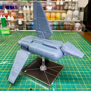 May include: A gray plastic model of a Star Wars spaceship with a detailed design. The spaceship is on a black base with a white starfield pattern.